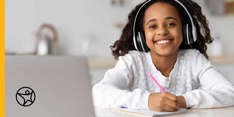 Online middle school student in a white sweater with a laptop and a pink pen taking on online class from home.