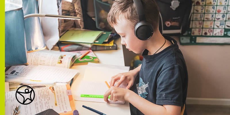 Elementary student in a blue t-shirt and headphones using a music playlist to help concentrate while talking an online summer class at Connections Academy.