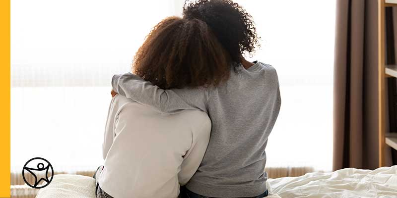 Image of a mother in a grey shirt giving her child in a white shirt a comforting hug.
