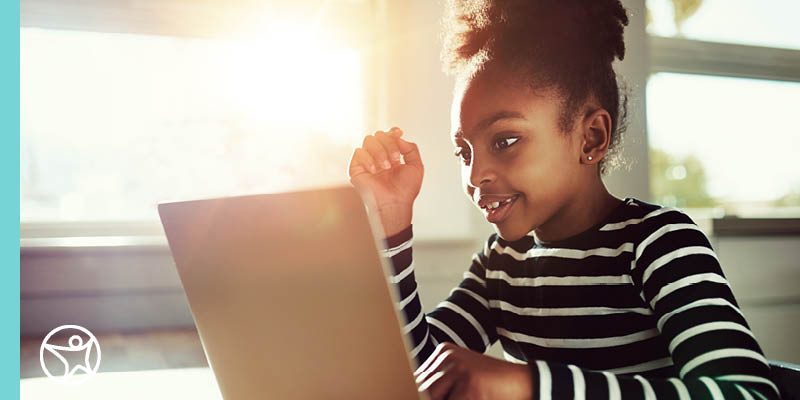 A young elementary student taking on an online class for Ohio Connections Academy on her laptop wearing a black and white long sleeved t-shirt.
