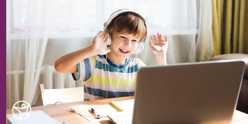 Young male student smiling holding his hands up an an online teacher at Connections Academy during an online elementary class.