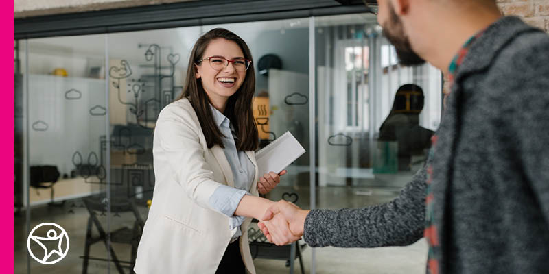 Image of a smiling young female teen in a white suit coat working in an office environment extending her hand out for a handshake.