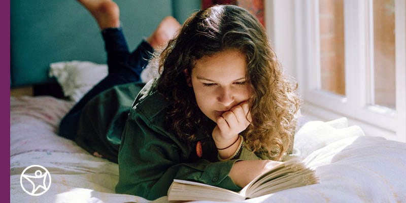 middle school girl reading a book on her bed