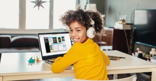 An online student in yellow sitting at a desk on a laptop participating in an independent learning activity