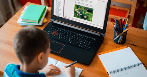 An image of a boy sitting at his desk working on his online class assignments. 