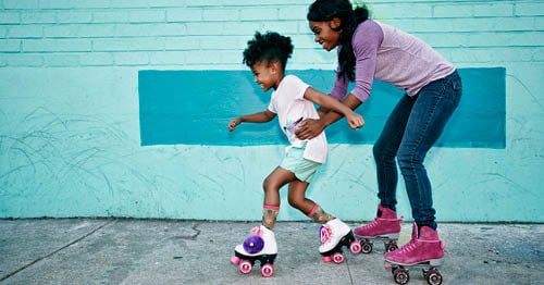 A parent helping her child roller skate as a summer activity for kids. 