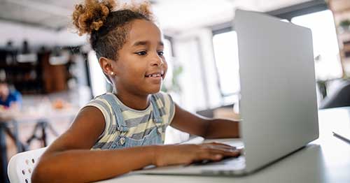 An online student sitting at a table and learning about computers for beginners.