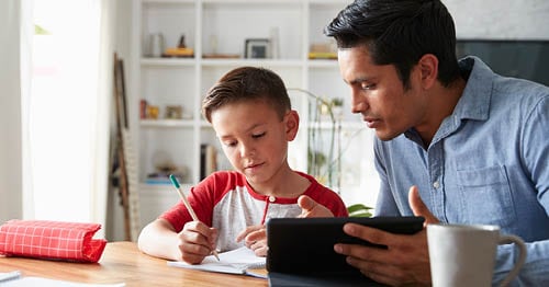 Image of a young male Connections Academy student sitting with his dad writing in a notebook.