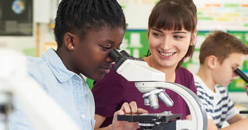 A student in a blue shirt looking through a microscope.