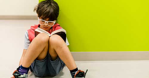 Youg elementary sudent reading a book against a green wall.