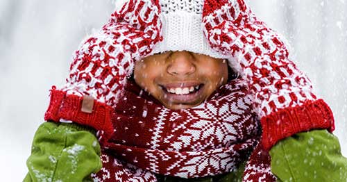 An online student smiling in a red and green sweater playing in the snow. 