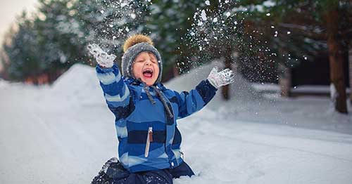 An online student smiling in a blue sweater playing in the snow.