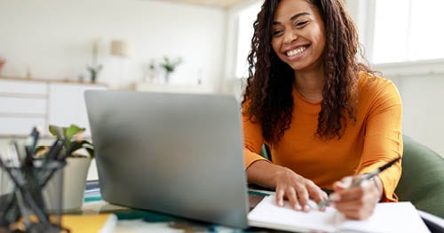 A teenage girl is taking notes while particpating in an online class