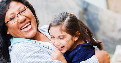 Image of an indigenous woman and her daughter hugging each other and smiling happily. 