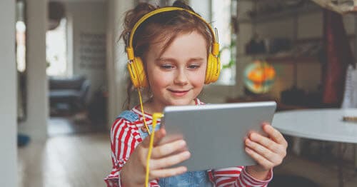 An elementary school student is listening to music on an ipad with yellow headphones