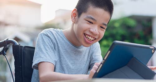 An online school student, who uses a wheelchair, studies for school on a tablet. 