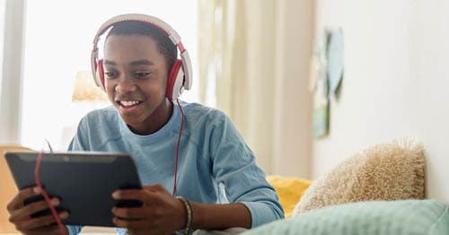 Young student in a blue shirt and red headphones is chatting with his online friends from his online classes at Connections Academy.  