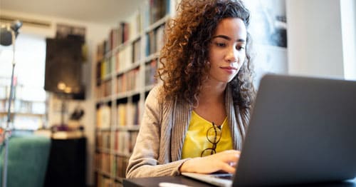 Young student in a yellow shirt working on an online school class at home in her study. 