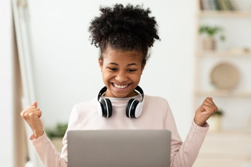 An online school student wearing a white shirt smiling at a computer seeing her learning progress brought to life through gamification in school. 