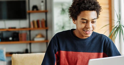 Young male student in a blue and red shirt looking at his laptop taking an online class at Connections Academy. 