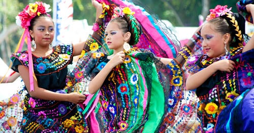 3 young students celebrating a traditional dance in dresses featuring bright and bold colors.