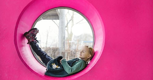 Young student at a park laying down in a pink tube. 
