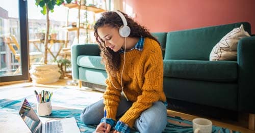 A student wearing a mustard color sweater using a laptop to research about gamification.  