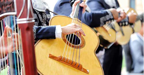 Image of a person in traditional Hispanic clothing playing Spanish guitar.