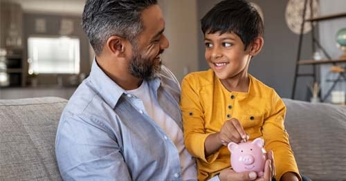 Young student in a yellow shirt is looking at their father holding a pink piggy bank