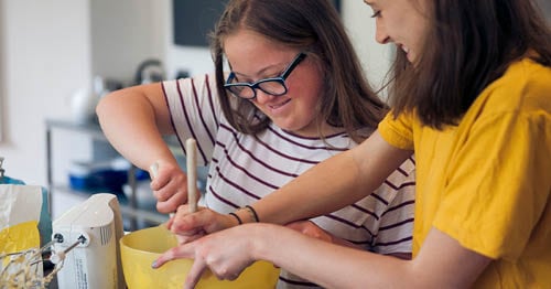 Image of two young Connections Academy students, a girl in a yellow shirt and another girl in a striped shirt, making a health dish together.
