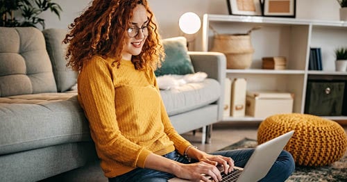 A student wearing a yellow shirt sitting at a laptop working on an online assignment for Connections Academy. 
