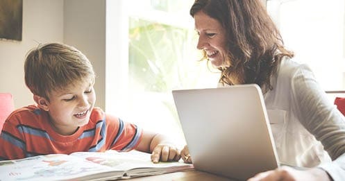 Young student in a red and blue striped shirt is working on an assignment with his learning coach mom. 