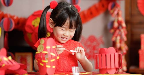 Young Connections Academy student during Chinese New Year wearing red and making a craft. 