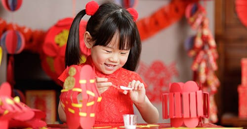 Young Connections Academy student during Chinese New Year wearing red and making a craft.