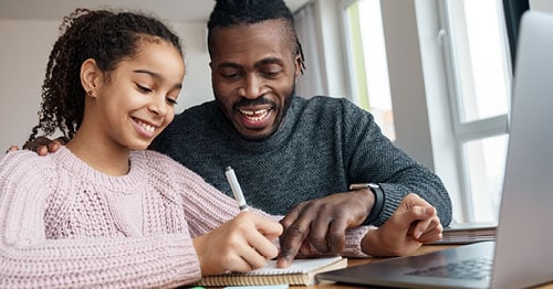 A 9th grader in a pink shirt smiling doing research towards an accredited online school like Connections Academy with her learning partner/dad. 