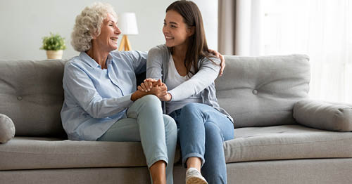 Image of a young female Connections Academy student in a white shirt sitting with her grandmother. 