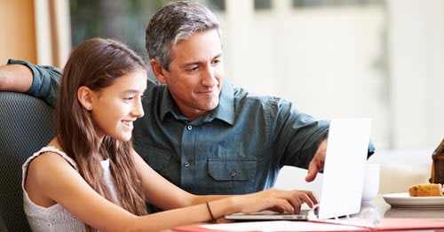 Middle shool girl learning online with her father assisting