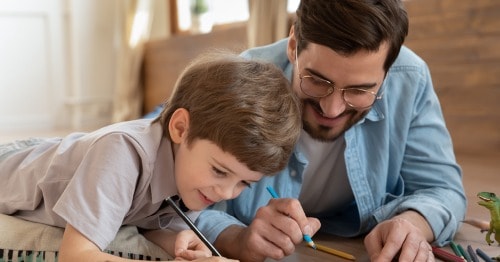 A male parent helping an elementary-aged male student with their writing assignment