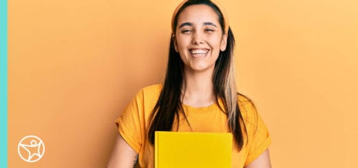 Connections Academy student against a yellow wall smiling holding a yellow notebook.
