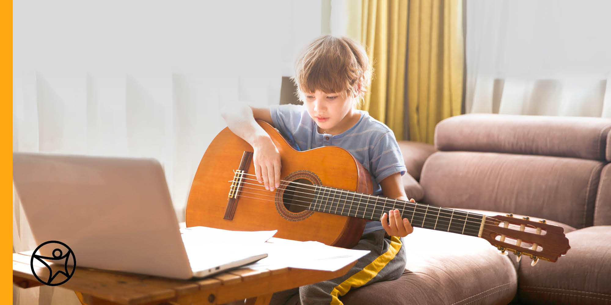 middle school boy plays guitar in front of laptop and sheet music