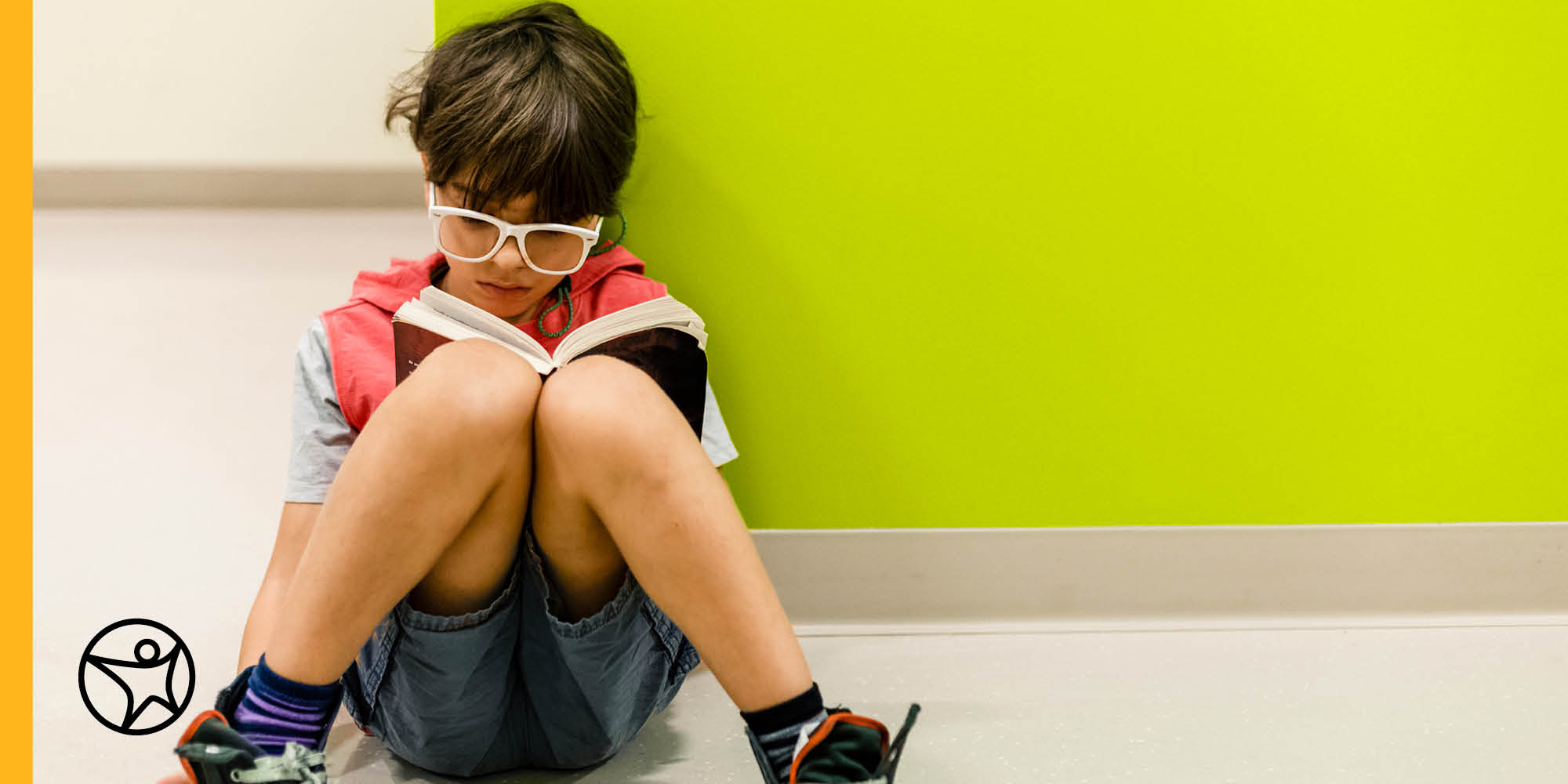 young boy sits on floor reading book