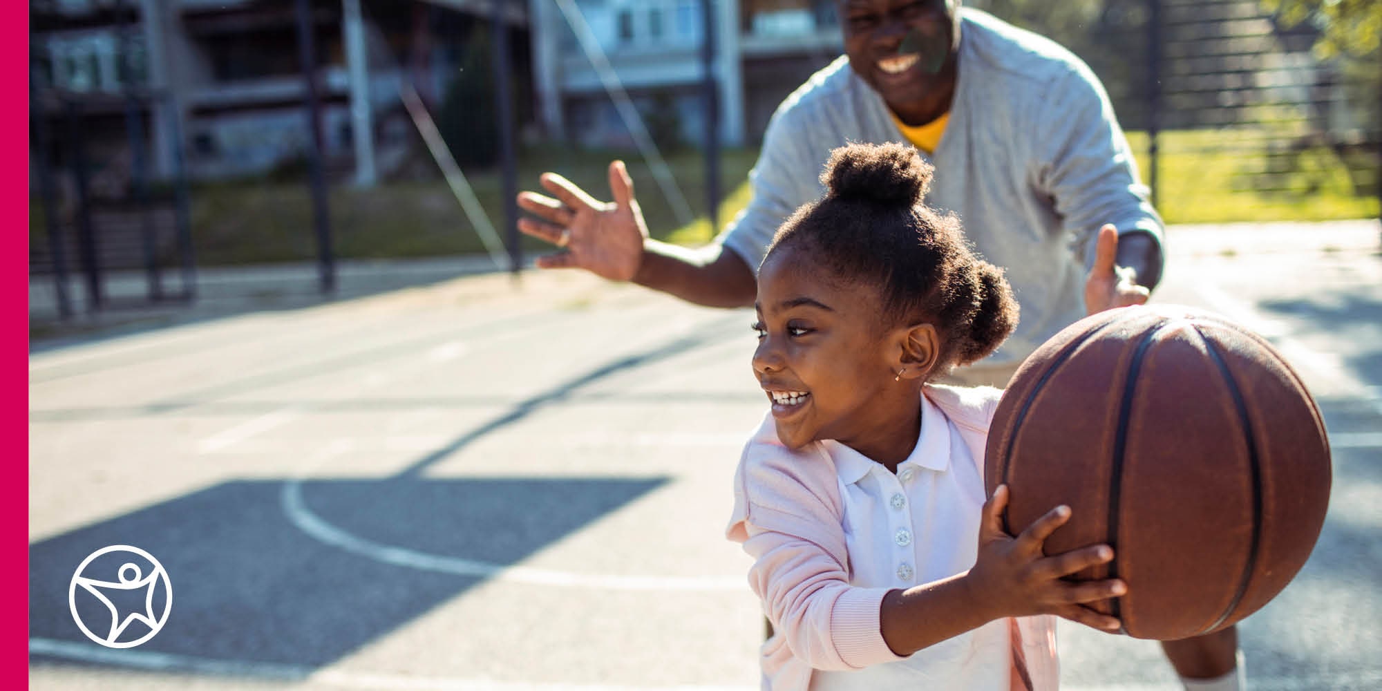 A young girl is playing basketball with her dad