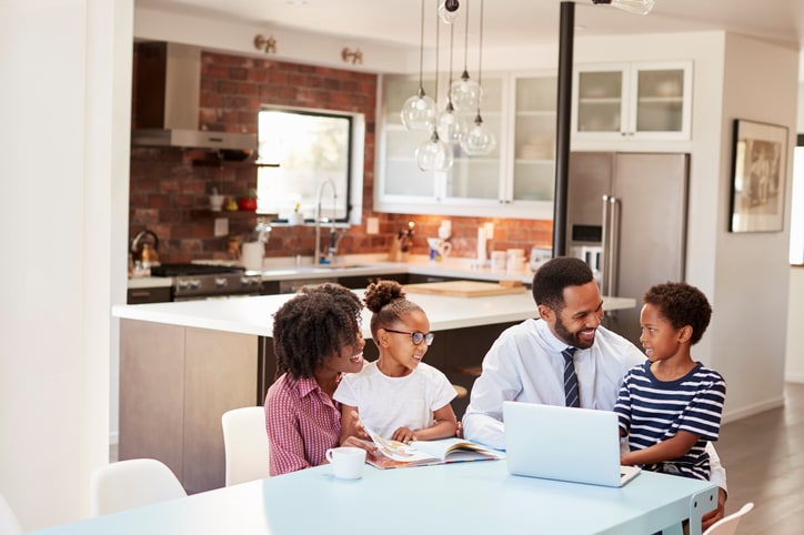 Parents Sitting Around Table At Home Helping Children With Homework