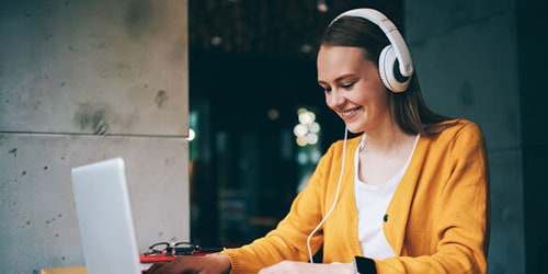 Female student in headphones looks directly at camera to support how listening to music helps students