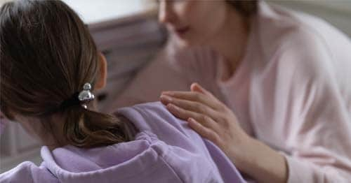 Mother comforting daughter by rubbing her back while talking