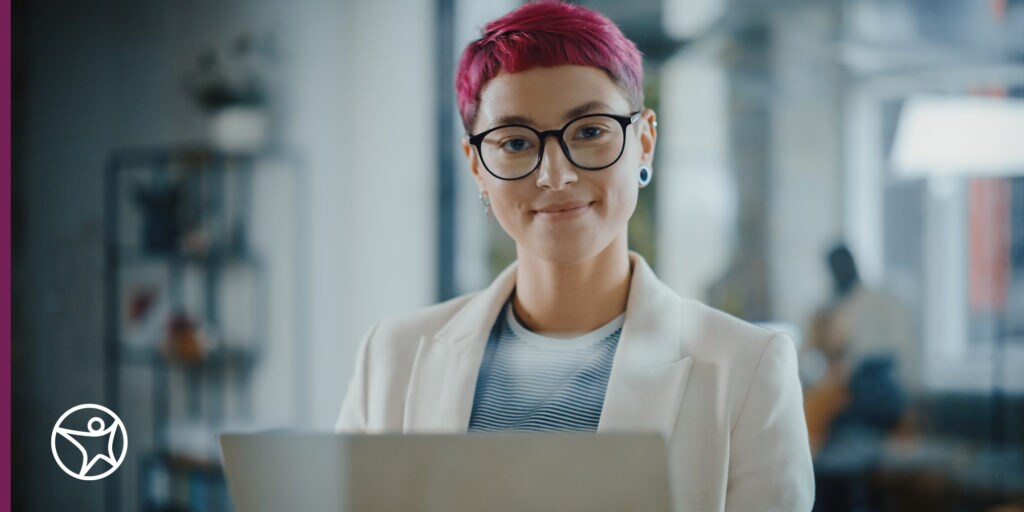 A teenage girl with pink hair smiling with a laptop