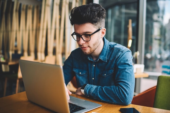 A teenage boy is sitting down and looking at a laptop