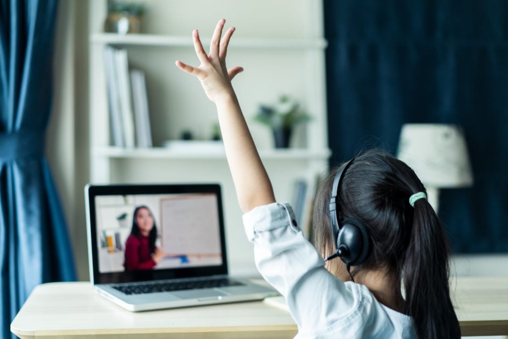 A young girl is raising her hand during an online class