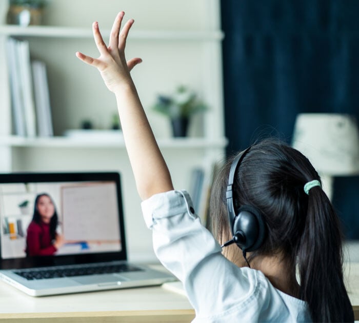 A young student raising her hand in her online class
