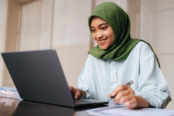 Image of a student in a green hijab sitting at a desk with her laptop working on an online assignment for a Connections Academy online math class. 